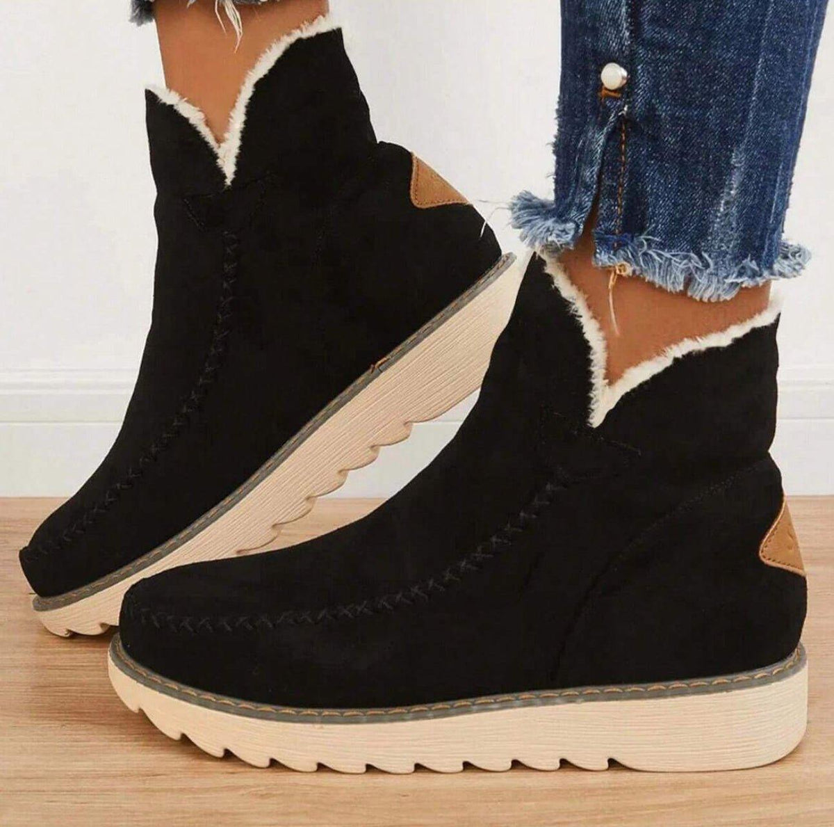 Black suede-look ankle boots with cream fleece trim and chunky cream sole, seen from the side on a model wearing frayed jeans. 1