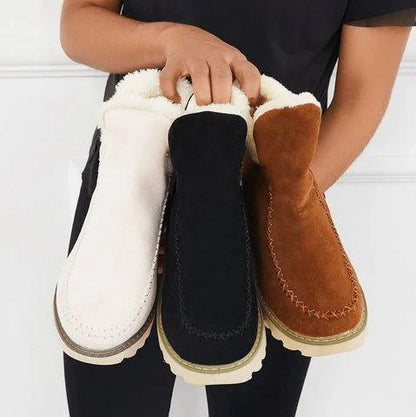 Three fleece-lined ankle boots in cream, black and tan held together in a model's hands, showing the colour options. 7