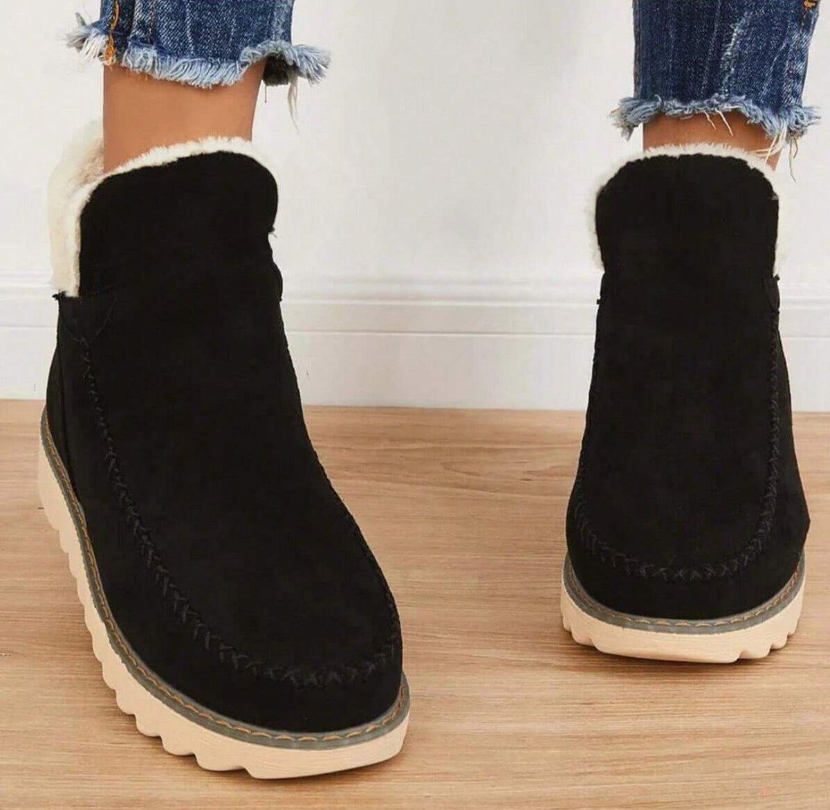 Front view of black ankle boots worn by a model, showing the rounded toe, decorative stitching and fleece-lined opening. 4