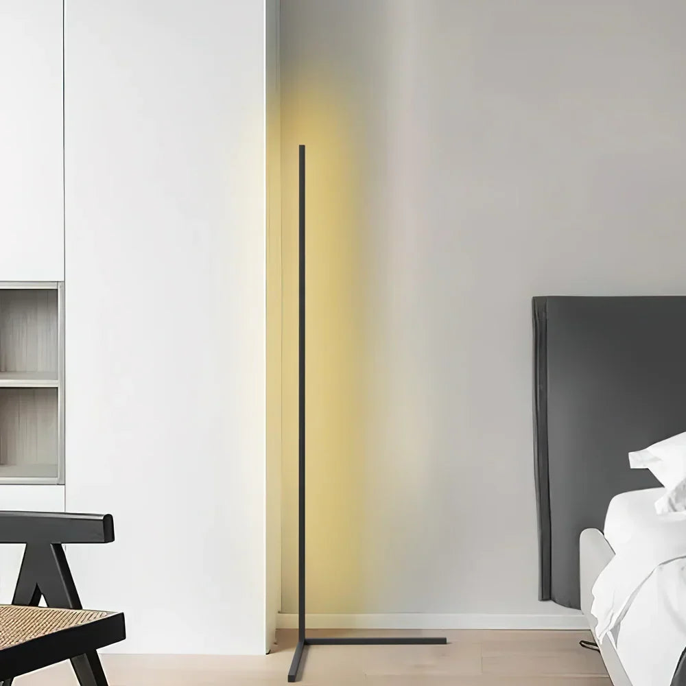 Black L-footed lamp glowing pale yellow in a bright white room beside a bed headboard 7
