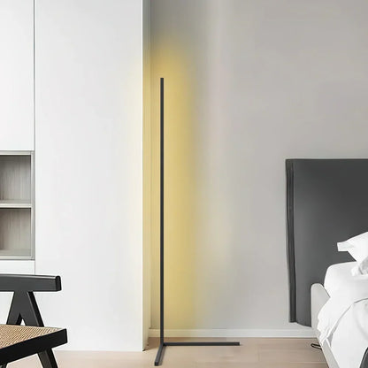 Black L-footed lamp glowing pale yellow in a bright white room beside a bed headboard 7