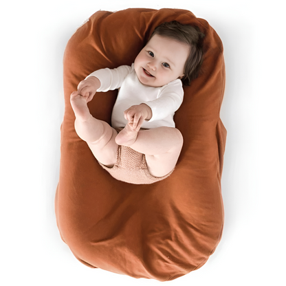 Baby in a white bodysuit holding their feet, lying in a rust-brown lounger 7