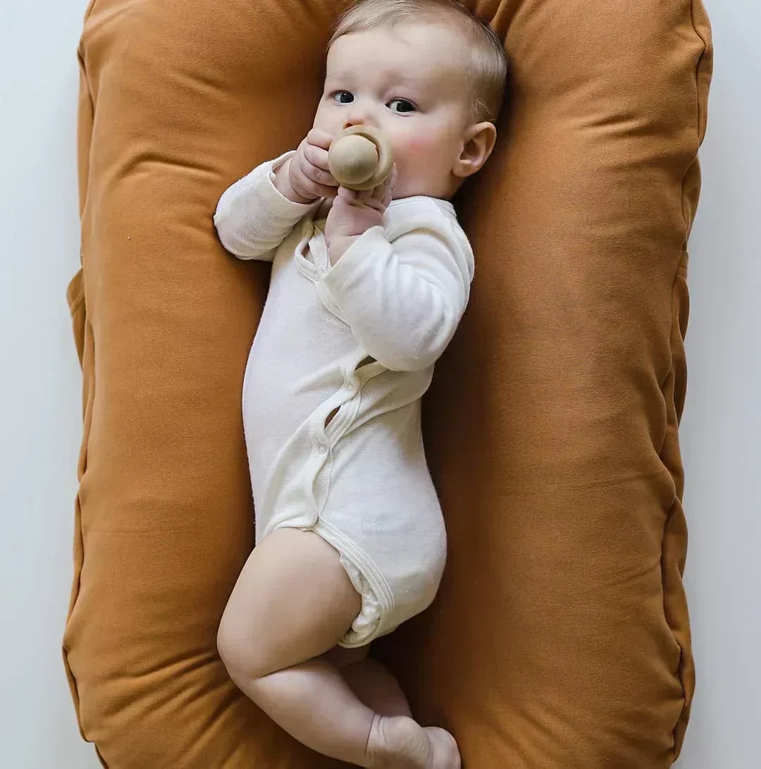 Baby in a white bodysuit holding a wooden teether in a rust-orange lounger 4