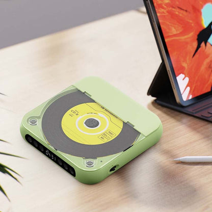 Green player with a yellow disc visible under its lid, on a desk beside a tablet in a case and a stylus. 12