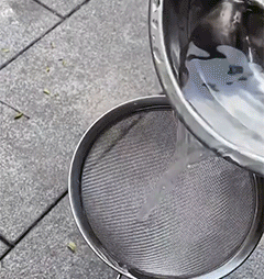 Clear liquid being poured from a metal bowl onto a mesh sieve over paving slabs 10