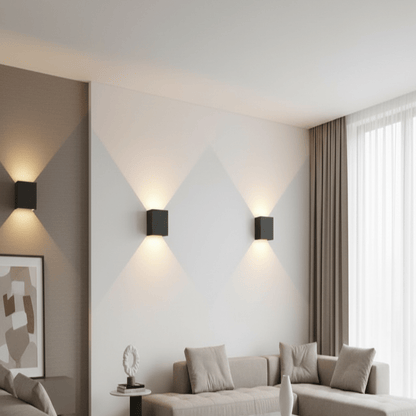 Three black cube wall lights casting up and down beams in diamond patterns across a pale living room wall beside a sofa. 1