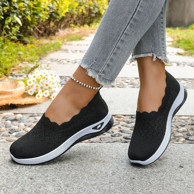 Black knit slip-on shoes worn mid-stride with frayed grey jeans, daisies and a straw hat in the background 14