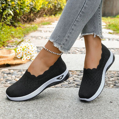Black knit slip-on shoes worn mid-stride with frayed grey jeans, daisies and a straw hat in the background 14