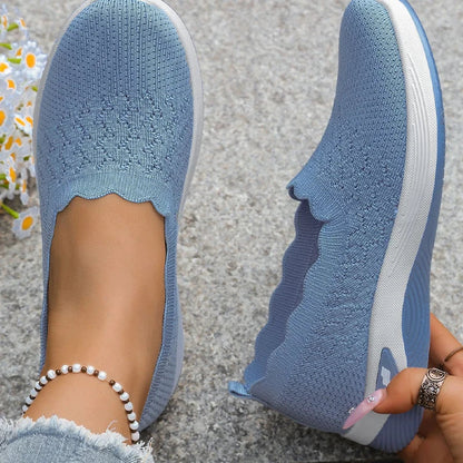 Top-down view of blue knit slip-ons showing the scalloped collar and perforated pattern, one shoe tilted by hand 16