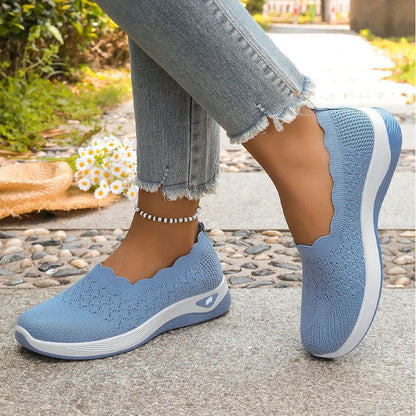 Blue knit slip-on shoes worn with frayed grey jeans on a paved path, daisies and straw hat nearby 17