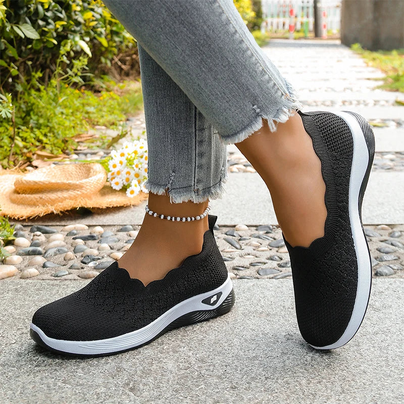 Black scalloped-collar knit slip-ons worn on a stone path, one foot angled to show the side of the shoe 15