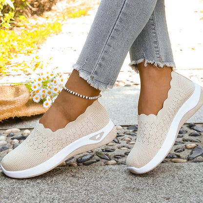 Beige scalloped-collar knit slip-ons worn with frayed grey jeans, seen from the side on a pebble path 8