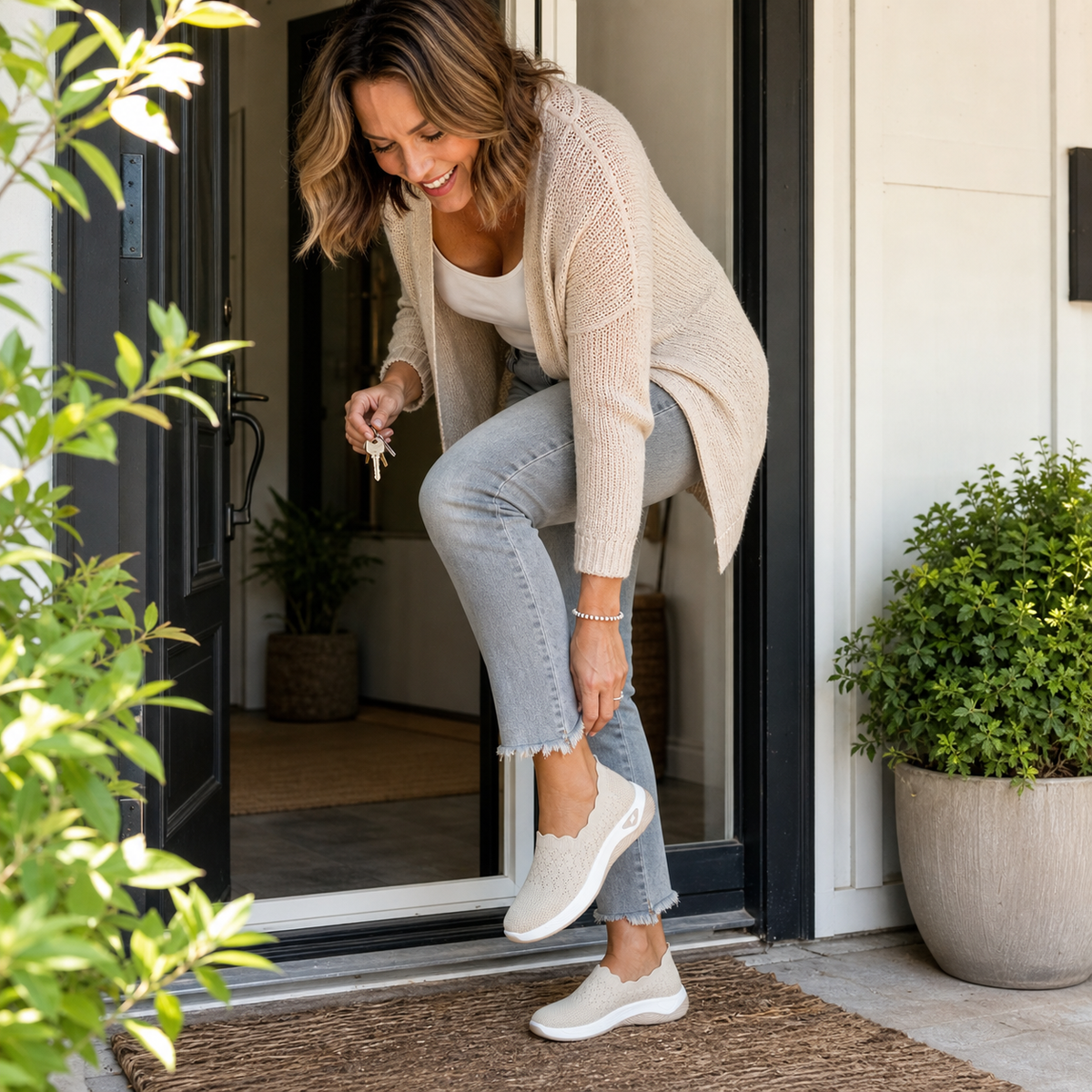 Woman in a cream cardigan leaving her front door, pulling on a beige slip-on shoe while holding keys 6