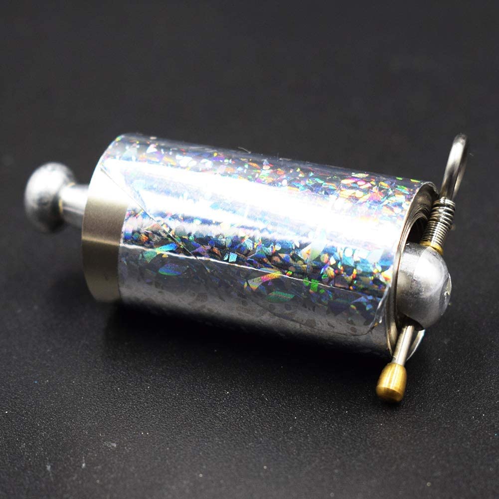 Close-up of the collapsed wand cylinder with holographic wrapping, ring pull, spring and brass-tipped pin on a dark surface 5