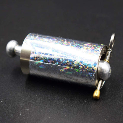 Close-up of the collapsed wand cylinder with holographic wrapping, ring pull, spring and brass-tipped pin on a dark surface 5