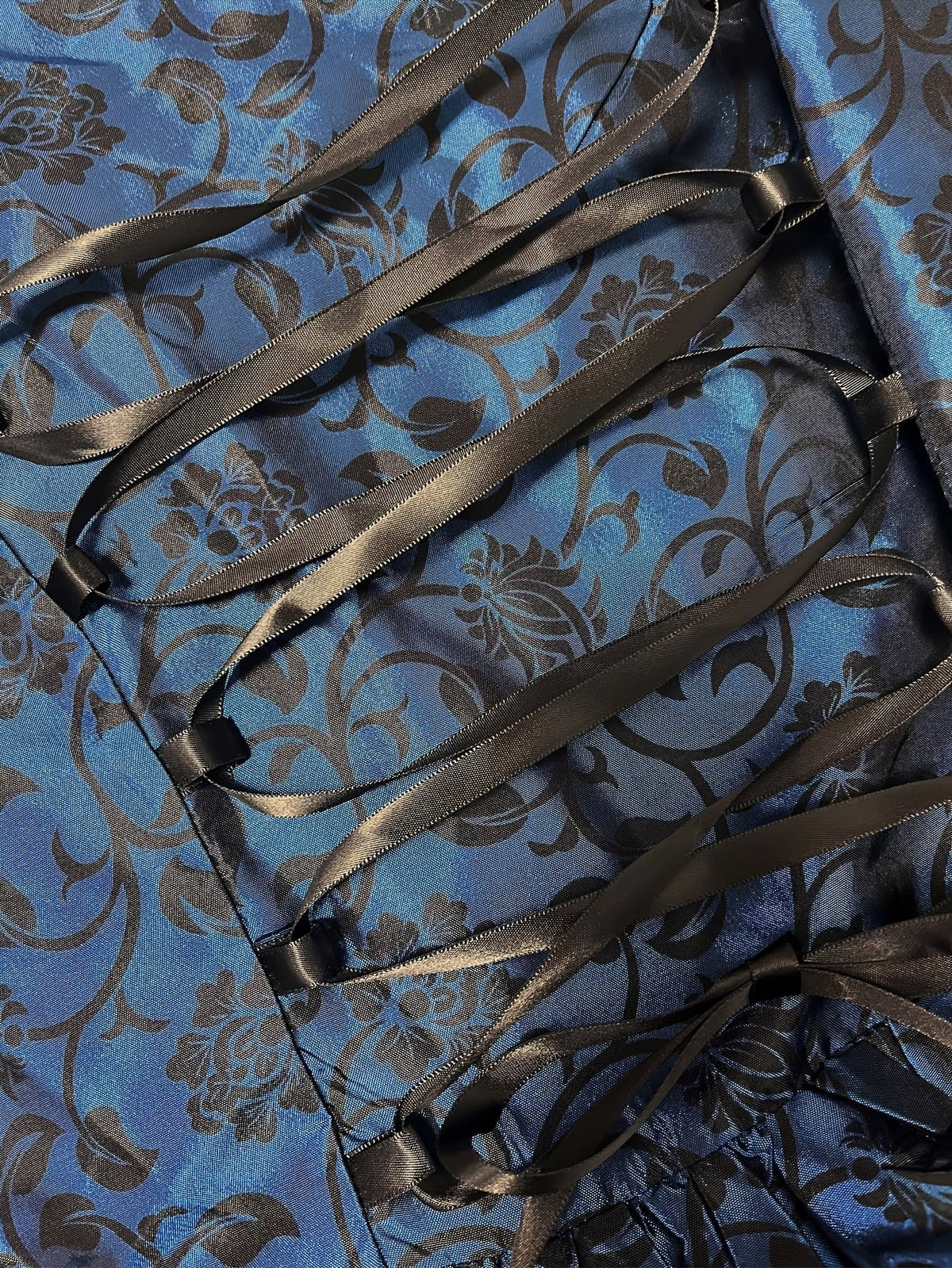 Close-up of the blue floral brocade fabric with black satin ribbon lacing and bow at the back of the gown. 5