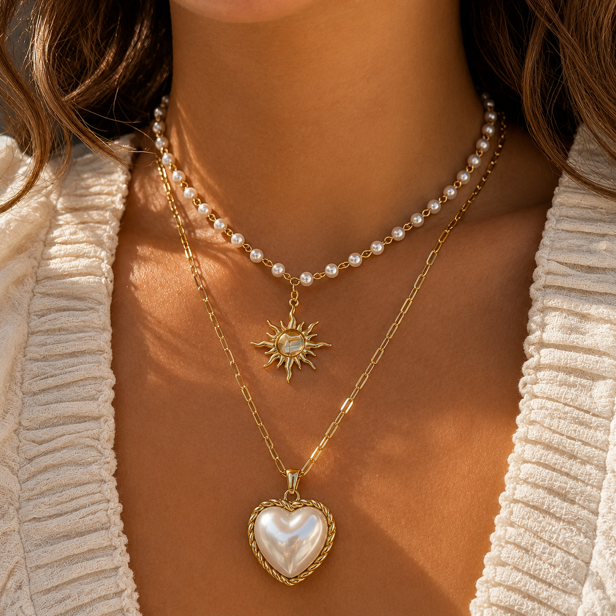 Worn by a model, the pearl chain sun necklace layered above a longer gold chain with a pearl heart pendant. 3