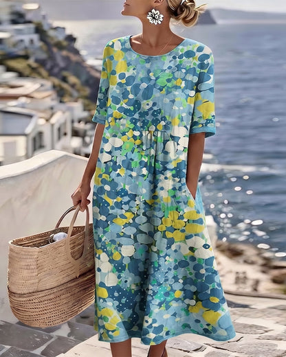 Model wearing the blue, yellow and green floral midi dress, carrying a woven basket by the sea 9