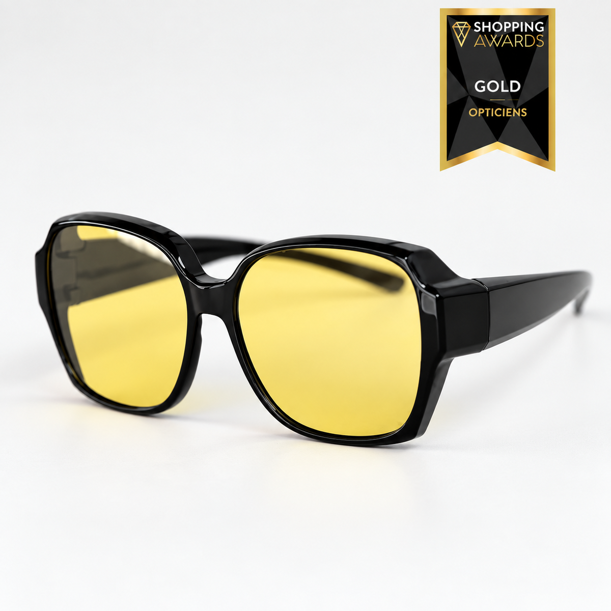 Oversized glossy black fit-over night driving glasses with yellow lenses, shown at a three-quarter angle on a white background. 1