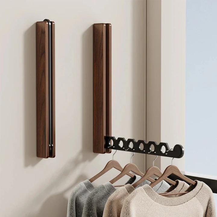 Two dark walnut-effect racks on a wall, one folded flat and one open, with jumpers hanging on wooden hangers. 7