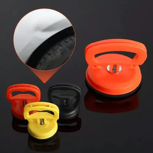 Orange, yellow and black suction pullers in different sizes on a dark surface, with an inset showing a small dent above a car wheel arch. 2