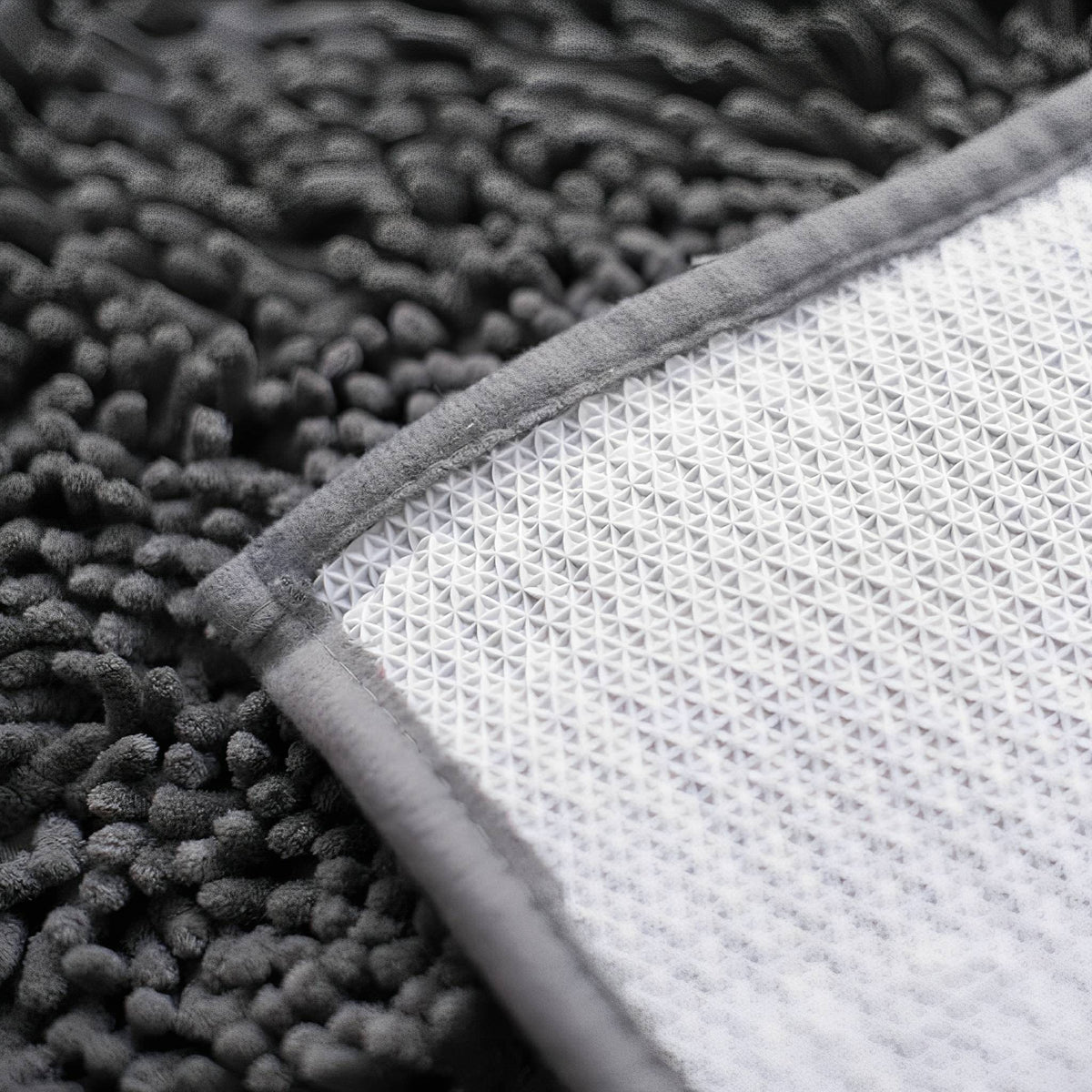 Corner of the mat turned over, showing the white textured non-slip backing, grey fabric edging and dark chenille pile. 8