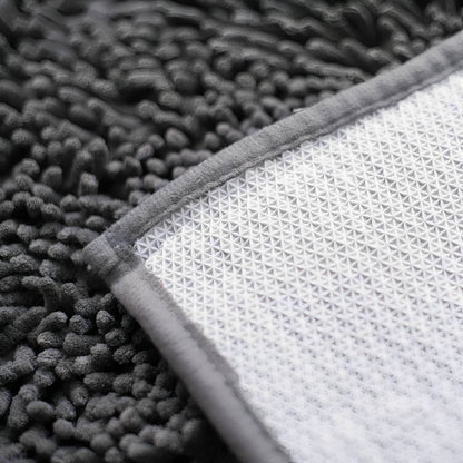 Corner of the mat turned over, showing the white textured non-slip backing, grey fabric edging and dark chenille pile. 8