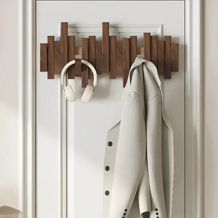 Dark wooden rack mounted on a white panelled door, holding white headphones and a pale coat 2