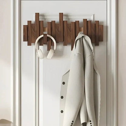 Dark wooden rack mounted on a white panelled door, holding white headphones and a pale coat 2