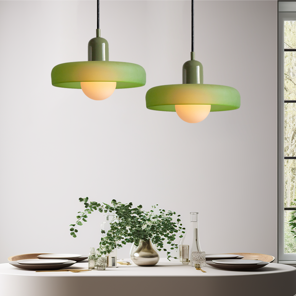 Two green pendant lights glowing warmly above a dining table set with plates, glassware and a vase of greenery 55