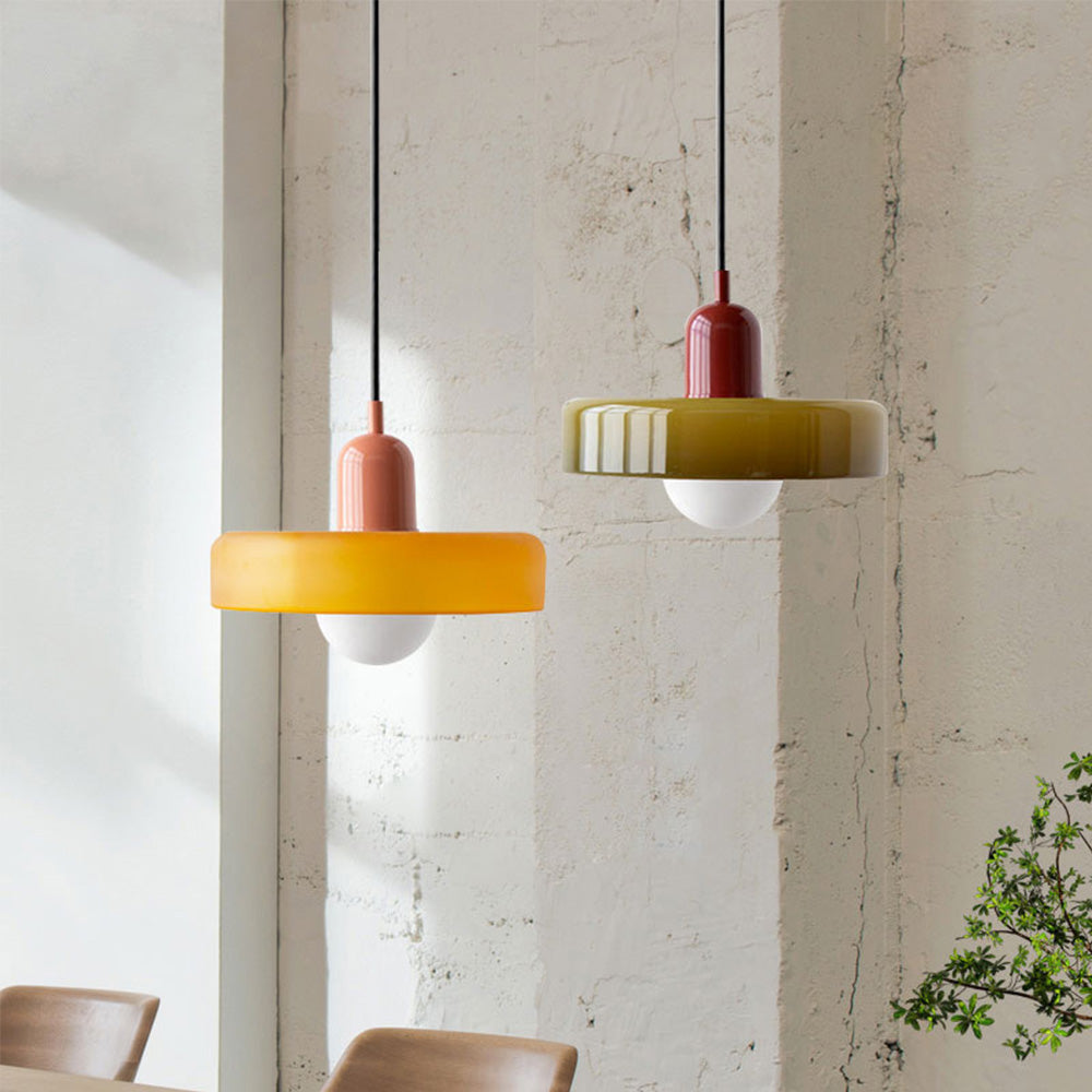 Two pendant lamps, one amber with a coral cap, one olive with a red cap, by a concrete wall 2