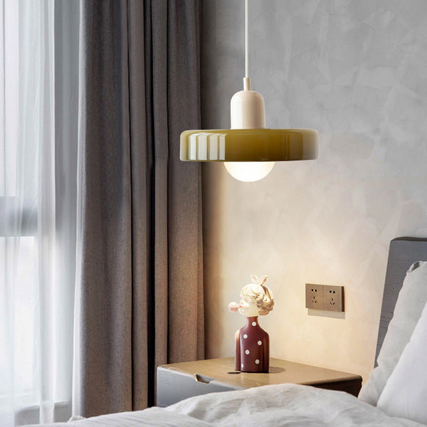 Olive glass pendant with cream cap and white cord lit beside a bed and grey curtains 15