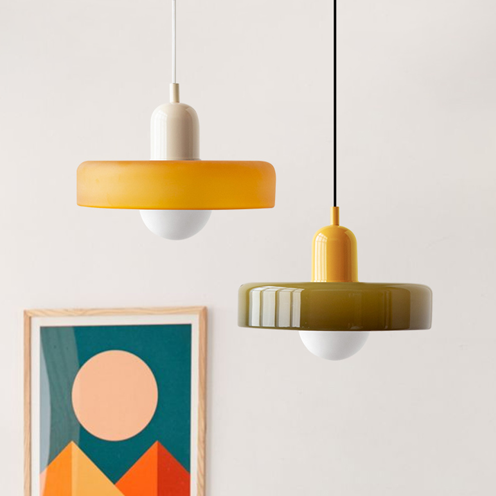 Two pendants hanging together, one amber with a cream cap, one olive with a yellow cap, above framed art 27