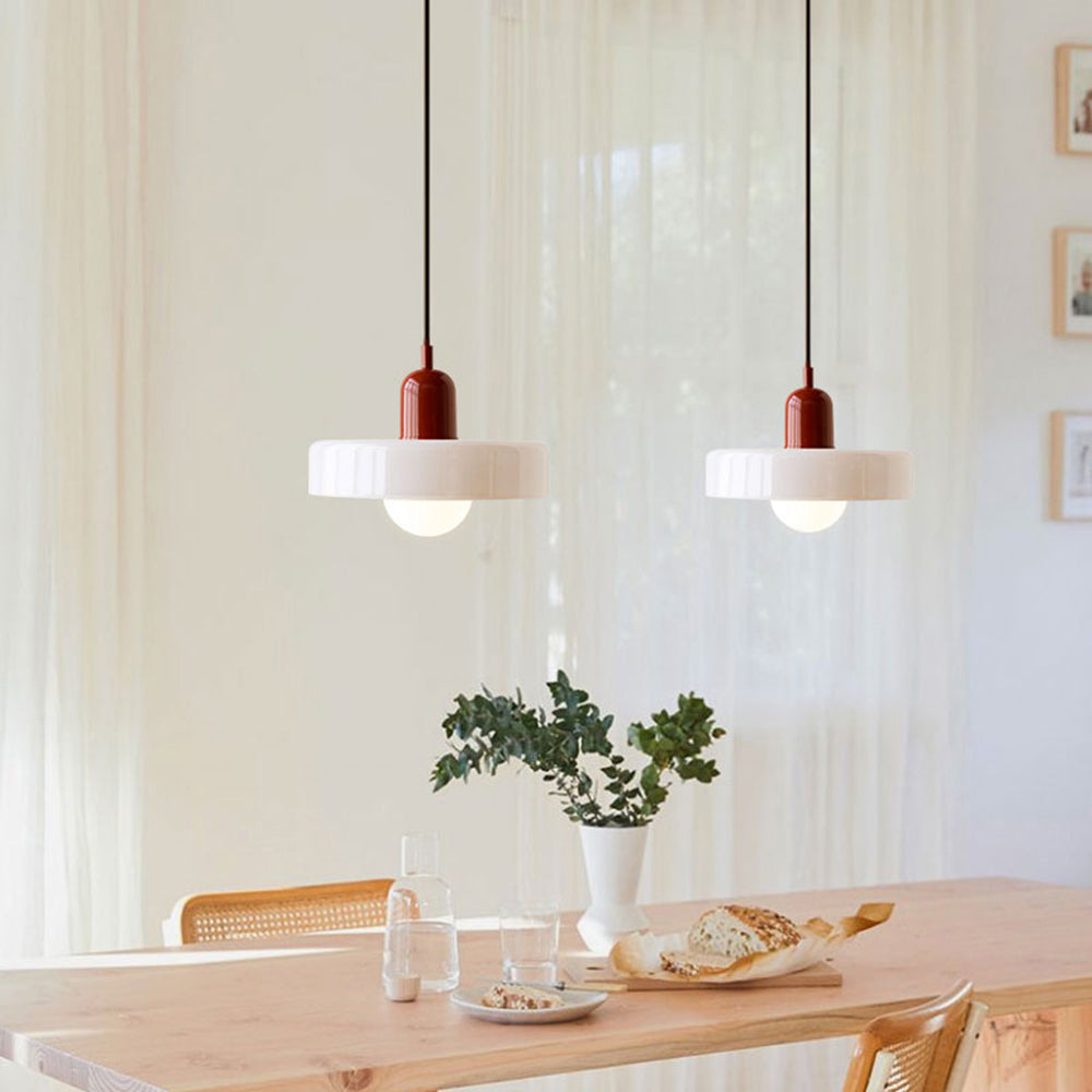 Two white glass pendants with deep red caps hanging above a light wooden dining table by sheer curtains 34