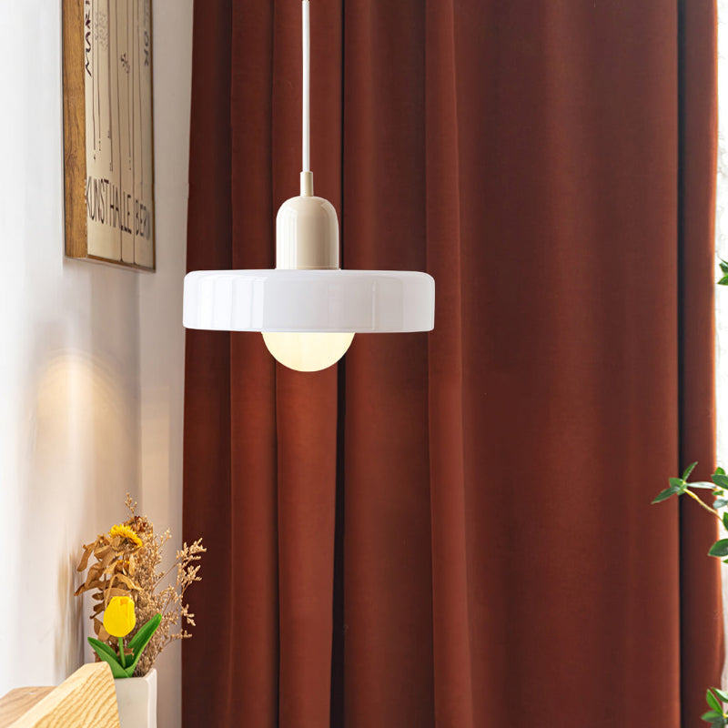 White glass pendant light with a cream cap hanging in front of rust-red curtains, near a small vase of flowers 47