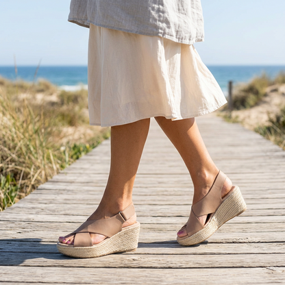 Taupe crossover wedge sandals with braided jute soles, worn while walking along a seaside boardwalk 1