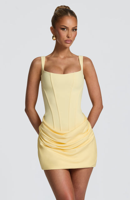 Close front view of the pale yellow dress on a model, showing the seamed corset-style bodice and draped hip detail. 22