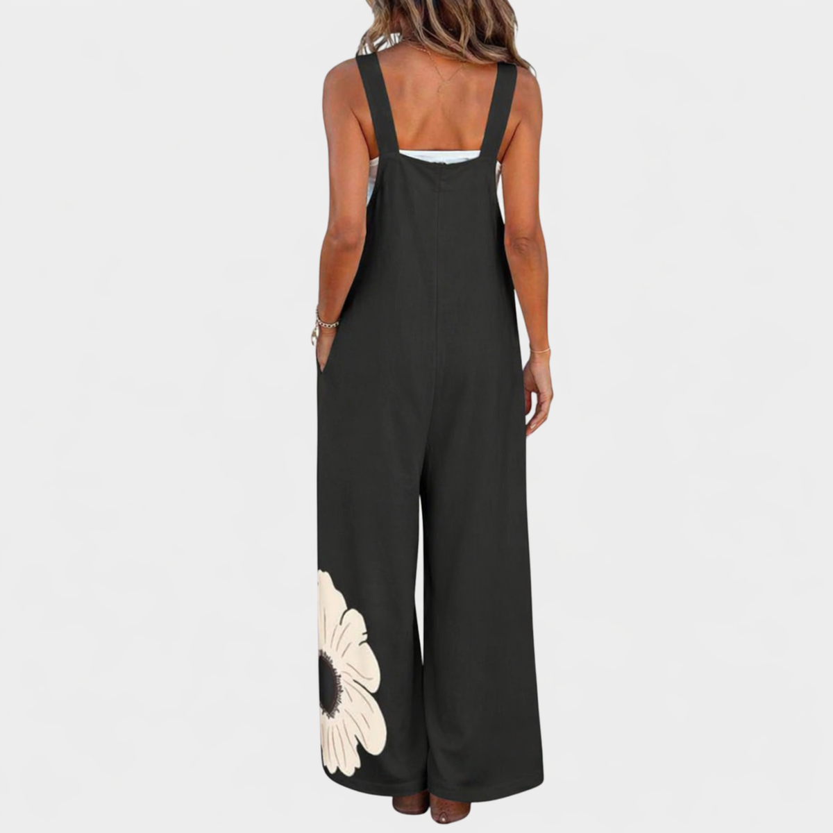 Back view of black wide-leg dungarees with broad straps and a cream flower at the hem 3