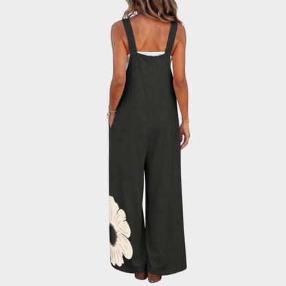 Back view of black wide-leg dungarees with broad straps and a cream flower at the hem 3