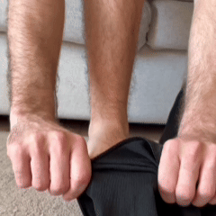 Close-up of a man's hands pulling dark fabric over his ankle in a living room 5