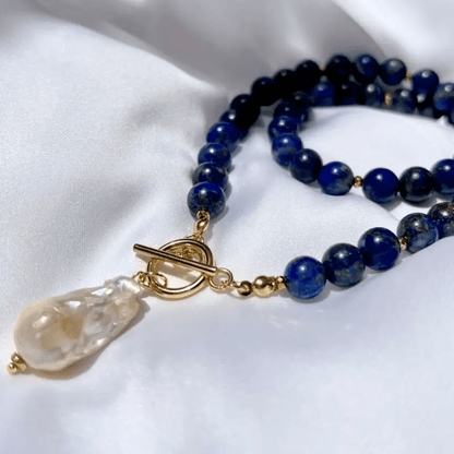 Gold toggle clasp and baroque pearl lying on white satin, with blue beads coiled behind 5