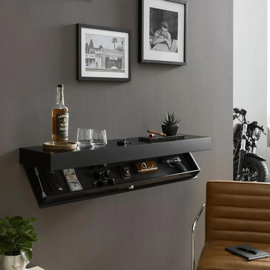 Black floating shelf on a grey living room wall above a leather chair, hidden compartment open and drinks displayed on top. 5