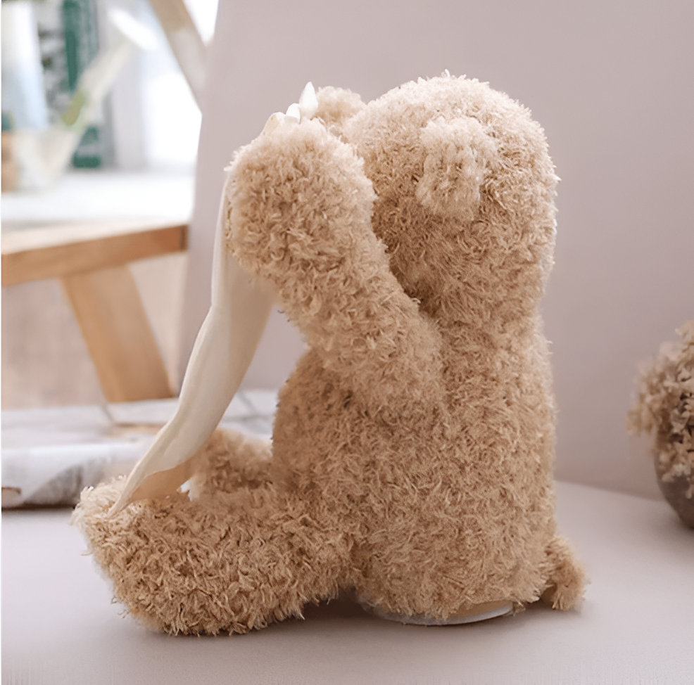 Side view of the teddy bear from behind, with one arm raised and the cream cloth hanging from its paw. 3