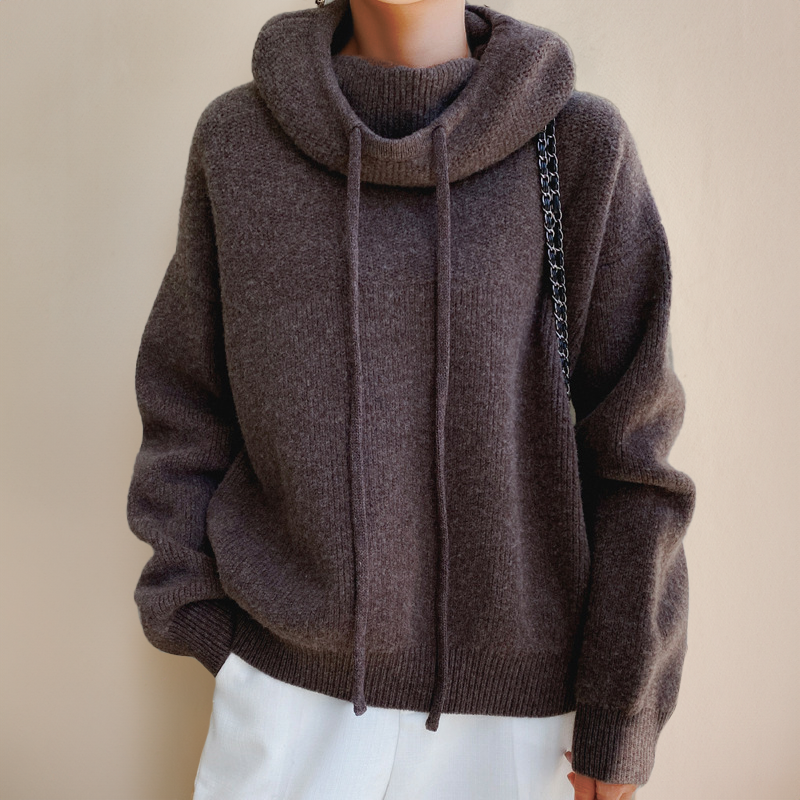 Front view of a brown ribbed jumper with a cowl hood, long drawstrings and white trousers 8