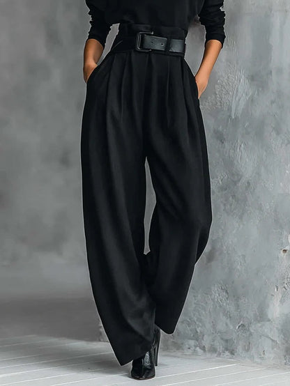 Detail of black pleated wide leg trousers with belt and side pockets, shown from the waist down 4