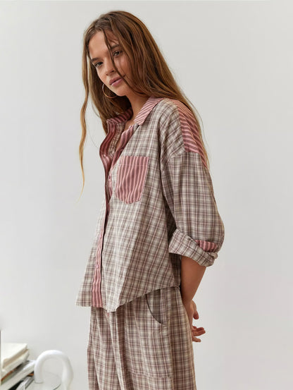 Model in the pink and beige check pyjama set with striped pocket and collar, turned side-on with one sleeve rolled up. 2