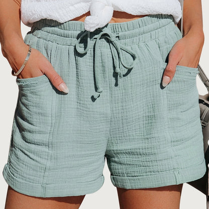 Model wearing the shorts in pale sage green textured fabric, hands in the patch pockets, with a tied drawstring waist. 5