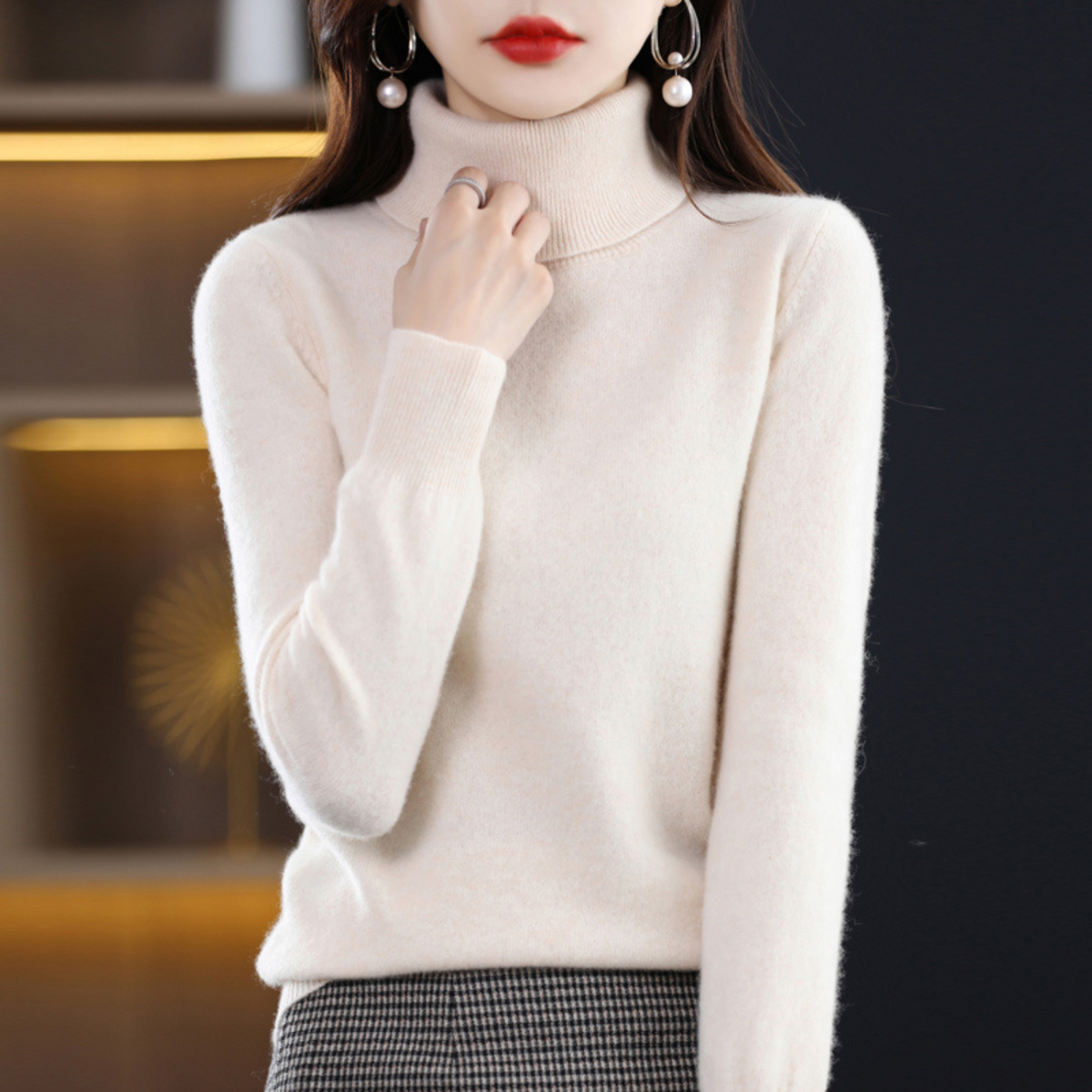 Ivory roll-neck jumper worn by a model with one hand at her collar, paired with a small houndstooth skirt. 15