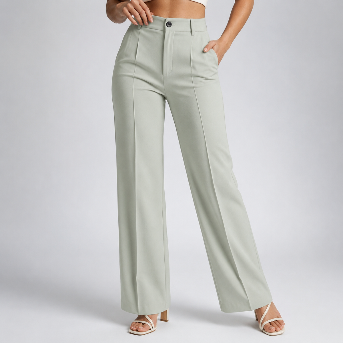 Model wearing pale sage-green trousers with a button fastening and pressed front creases, with cream strappy heels 23