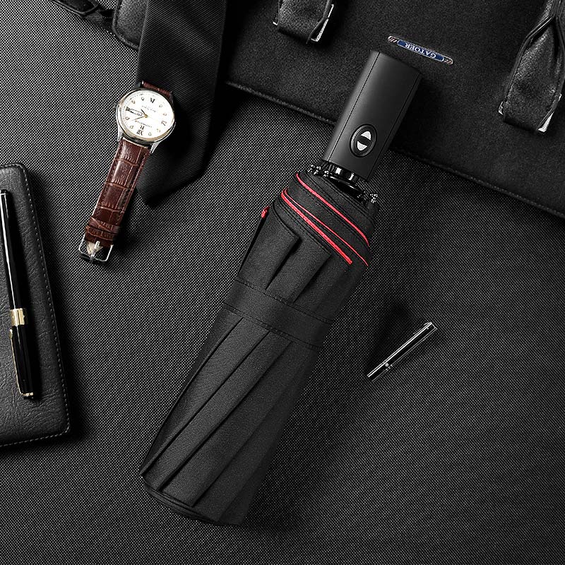 Folded black umbrella with red trim on a dark desk next to a watch, tie and pen 11